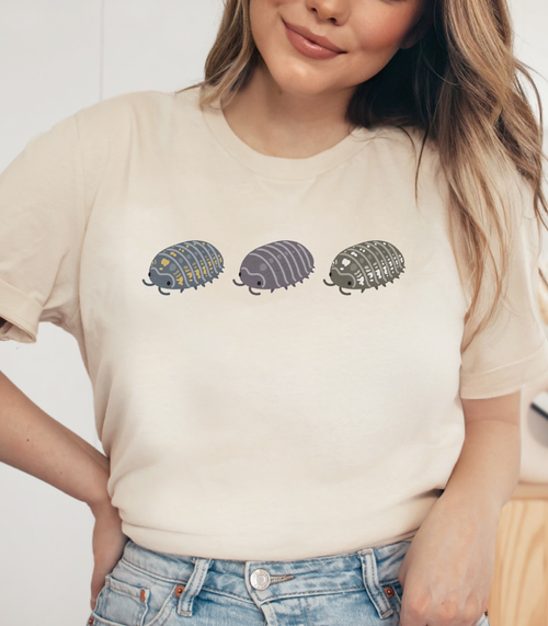 A women wearing a natural colored t shirt with a graphic of three stylized isopods in blue and yellow, purple, and black and white.